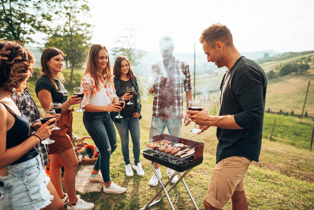 Junge Menschen stehen um einen Grill herum mit Weingläsern