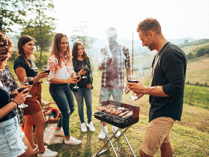 Junge Menschen stehen um einen Grill herum mit Weingläsern