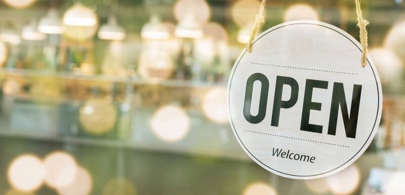 Rundes Schild mit den Worten "open" und "welcome" hängt an einer Glastüre mit Blick in ein Ladenlokal