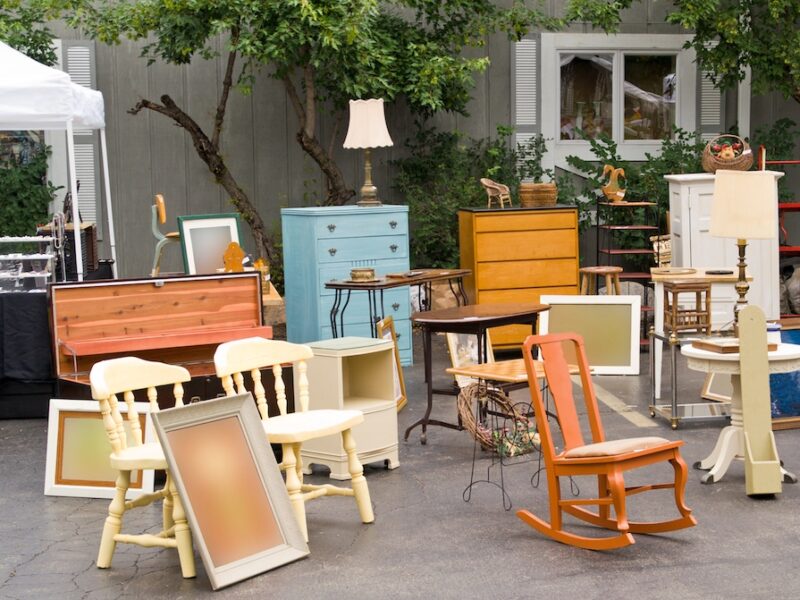 Bunte alte Möbel auf einem Flohmarkt vor einem Haus mit Baumbewuchs
